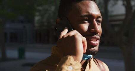 African american businessman with face mask talking on smartphone - Powered by Adobe