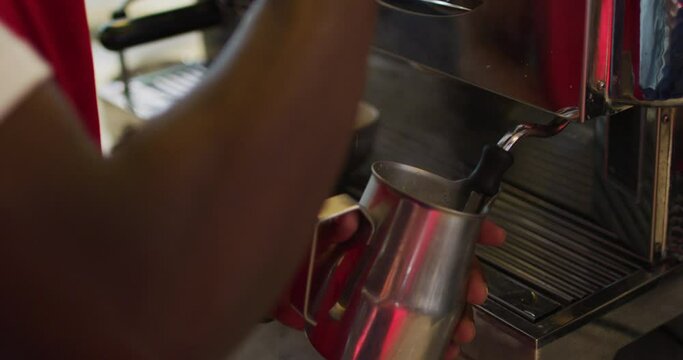 Midsection of african american barista using coffee machine frothing milk in cafe