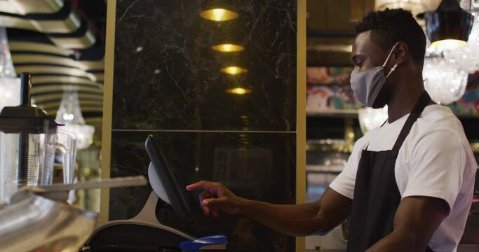 African american male barista wearing face mask using till
