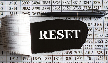 RESET is the word behind torn office paper with numbers and a black pen.