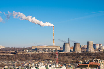 City in winter, the white smoke from pipe of the power plant rises among the houses, CHP heats houses