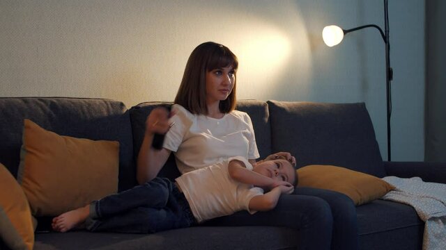 Happy family - mother with her little son sitting on the couch - the boy falls asleep on his mother's legs