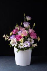 delicate bouquet of roses, lisianthus, daisies, chrysanthemums, unopened buds in a white round box on a gray table and black background.