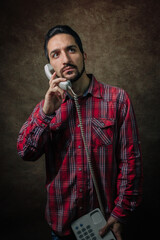 Portrait of a man. The man is talking on a landline phone. Man in red plaid shirt