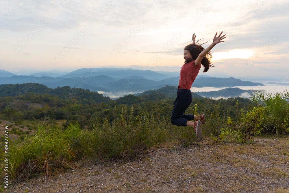 Wall mural happy asian woman traveler jumping at view point for sun light. travel lifestyle adventure concept