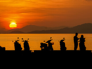 Silhouette of relaxing people and motorcycle with sunset background
