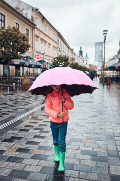 Little girl holding big pink umbrella walking in a downtown on rainy gloomy autumn day
