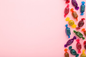 Colorful wrapped chocolate candies on light pink table background. Pastel color. Closeup. Empty...
