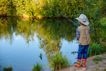 Child is fishing. Boy is a fisherman. Child with a fishing rod caught a fish in a pond. Nice catch!