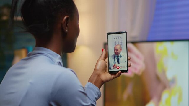 African famele having conference call with her doctor about illness treatment sitting in living room late at night. Black patient in a video call with medic discussing health problems of woman