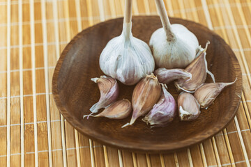 two heads of garlic and a clove unpeeled stands on a wooden plate