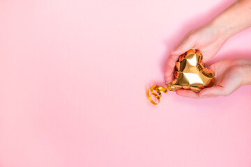 Female hands hold a gold heart-shaped balloon on a pink background. Valentine's day concept. Copy space for text.