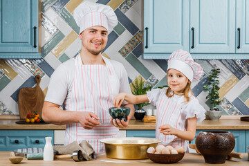 Cute little girl and her beautiful dad smiling while cooking in the kitchen at home. The concept of cooking