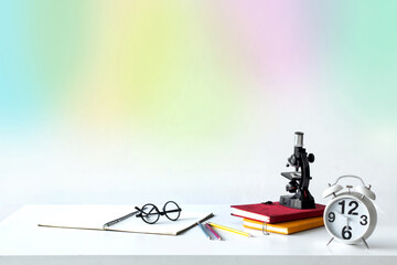Child's school desk with microscopes, textbooks, clock and eyeglasses are on the table, with multicolor background, back to school concept