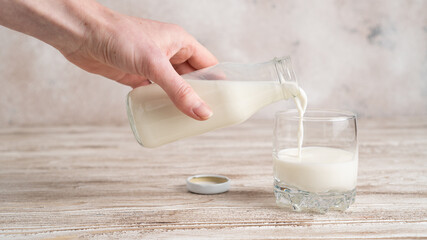 Glass bottle pouring milk into a glass on white background. Hand holding a bottle with milk on wooden table