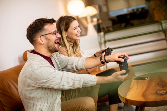 Young couple playing video games at home, sitting on sofa and enjoying themselves
