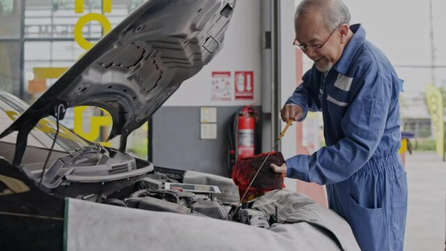 Professional Elderly Asian man mechanic wearing a uniform is checking engine oil. Service to customers. Professional Mechanic with factory work experience. Car maintenance business. Concept key worker