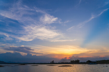 The sun shines through the clouds in the evening on a lake in Thailand.