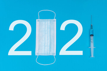 2021 logo made from a medical mask and a syringe with a vaccine. As a symbol of the pandemic and the release of the drug in 2021. Blue background