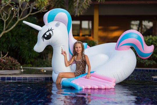 Cute funny girl sitting chilling on inflatable ring unicorn. Kid child enjoying having fun in swimming pool. Summer outdoor water activity for kids.