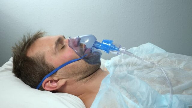 portrait of a man in an oxygen mask who lies on a bed in a hospital.