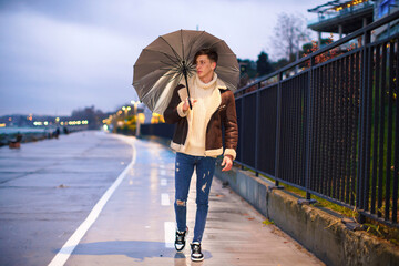 Man taking a walk in hand in the evening rainy weather. Young male taking an umbrella for a walk in the cold and rainy winter weather