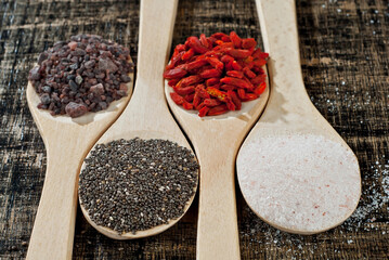 Goji berries, chia seeds, Tibetan black salt, pink Himalayan salt on wooden spoons. Spices on an old shabby board. Seasonings close up.
