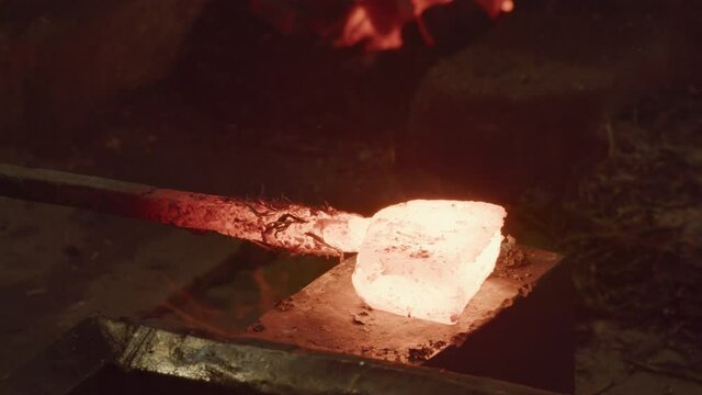 Red hot glowing ingot hammered on anvil then put back in coal forge, Blacksmith