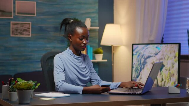 African american woman shopping online late at night sitting in living room with laptop using credit card. Employee making paymant transaction from home on digital notebook conected to internet