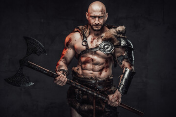 Barbaric bald and handsome viking warrior with muscular build and grimy skin posing in dark...