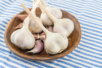 whole fresh garlic vegetable and slices on a plate standing on a striped tablecloth white and blue stripes