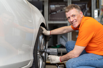 Male mechanic worker using pneumatic wrench changing tyre of car at auto repair shop. Professional...