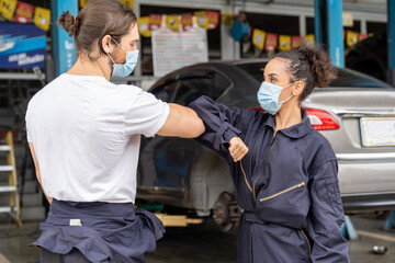Professional male and female mechanic worker wearing face mask for health and protect coronavirus or PM 2.5 greeting bumping elbows at auto car repair shop. Car repair service and health concept