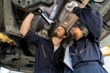 Fototapeta na wymiar Male and female car mechanic worker working using wrench tool for repair and maintenance underneath lifted car. Group of mechanic vehicle service maintenance checking under car condition in garage