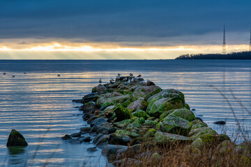 A beautiful sunset over the green boulders on a wave breaker. Photo from Hallevik, Blekinge county, Sweden