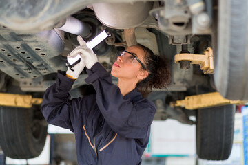 Female car mechanic worker working underneath lifted car. Female mechanic vehicle service...