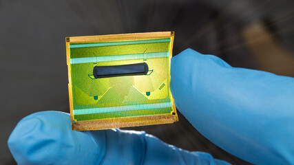 Close-up of flex circuit board in human fingers detail on dark background. Hand in blue glove...