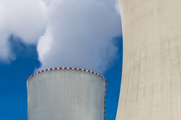 Detail of nuclear power plant cooling towers and white steam on blue sky background. Close-up of...