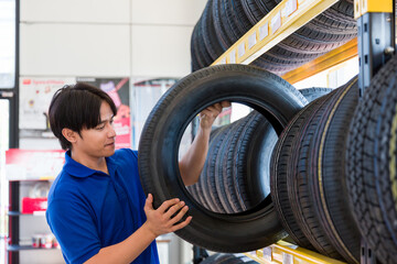 Car service. Asian male technician worker checking new tire wheel on shelves shelf at wheel store. Specialist mechanic examining new tire wheel. Car service and Maintenance concept