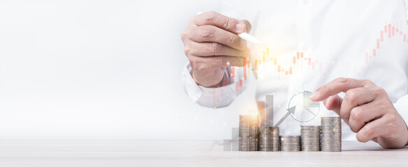 Hand of businessman holding stylus pen and pointing at graph on money coins stack. Panoramic of...