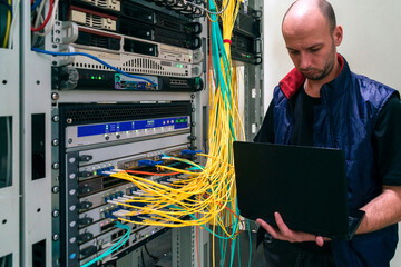 The system administrator with a laptop is in the server room. A man sets up a central router in a...
