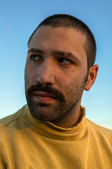 Fototapeta premium Portrait of young man with moustache looking away in front of blue sky wearing yellow jumper
