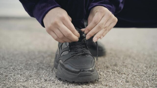 Close-up of female Caucasian hands tying shoelaces in sneakers. Unrecognizable sportswoman on morning training outdoors.
