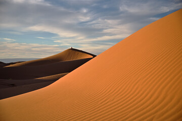 Fototapeta na wymiar Textur von Bergen von Sand in der Abendsonne mit einer Person auf einem entfernten Berg von Sand