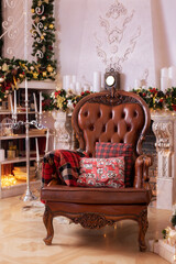 Stylish interior of room with Christmas fir tree and brown armchair. Beautiful cozy decorated living room for Christmas with fireplace. Holiday concept. Red pillows and checkered plaid on armchair.	
