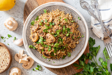 Quinoa stewed with mushrooms, onions, garlic, and parsley in a plate on a gray concrete background top view. Delicious and healthy vegetarian food. Quinoa with champignons.