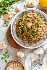 Quinoa stewed with mushrooms, onions, garlic, and parsley in a plate on a gray concrete background top view. Delicious and healthy vegetarian food. Quinoa with champignons.