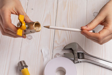 Woman plumber demonstrates gas stopcock with internal (female) thread. On white wooden background.