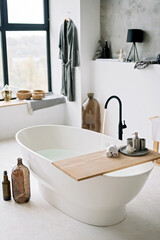 White bathtub fills with foam water in a modern apartment with stylish loft-style interior design, home decor. Spa concept, relaxation. Soft selective focus.