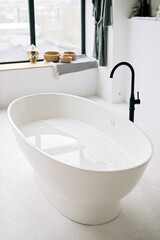 White bathtub fills with foam water in a modern apartment with stylish loft-style interior design, home decor. Spa concept, relaxation. Soft selective focus.